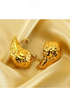 Macro detail of 18K gold hammered teardrop earrings on elegant yellow silk fabric