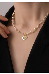 Gros plan d'un collier de perles français avec pendentifs soleil et œil en or 18k sur mannequin.