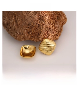 Macro shot of gold square stud earrings with vertical striped relief on a stone surface