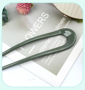 Detail view of a smooth dark green U-shaped hair pin for casual buns and styling