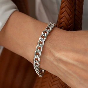 Close-up of a silver Cuban chain bracelet on a wrist with minimalist metal texture