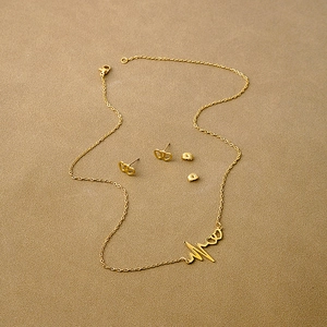 Detailed view of gold heart necklace and earring set on a textured brown background