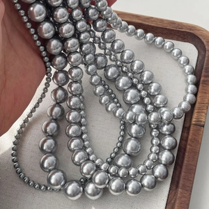 Close-up of multi-size metallic silver pearl necklaces on a linen tray display