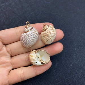 Close-up of three natural shell pendants with gold plated edges held in hand for DIY