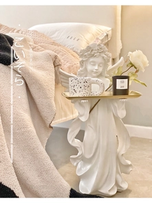 Detail of white resin angel sculpture holding a golden metal tray for storage