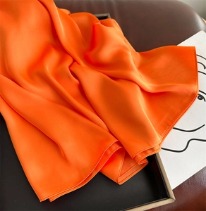 Close-up of elegant orange silk satin scarf folded neatly in a dark display tray