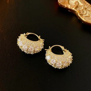 Close-up of golden handbag-style earrings with pave-set zircons on a textured black background