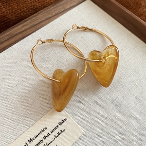 Detail of amber acrylic heart pendant on gold metal hoop earrings for women