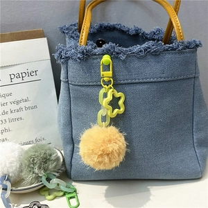 Detail of a denim handbag featuring a soft ginger faux fur pom pom flower keychain charm