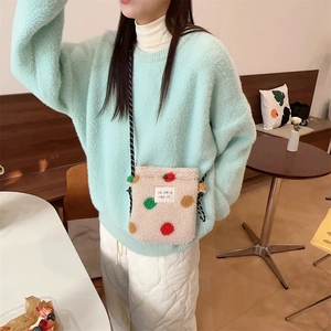 Détail du sac pelucheux à pois arc-en-ciel porté sur un pull vert menthe dans un café