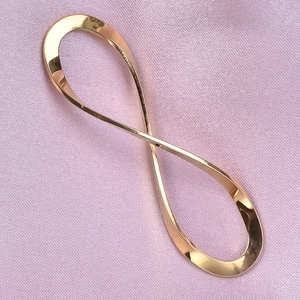 Detailed view of polished golden infinity symbol pendant on soft pink fabric background