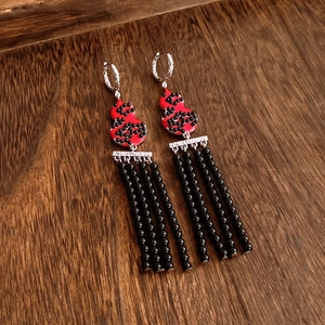 Detail of enamel gourd earrings with black beaded tassels on a vintage wood background