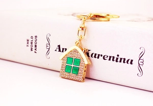 Close-up of golden house keychain with clear rhinestones and green square gemstones