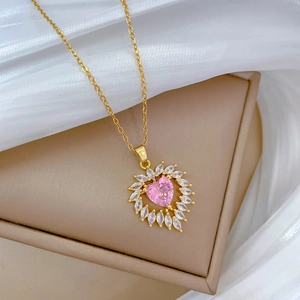 Macro shot of gold heart necklace with pink zircon stone on a beige jewelry box