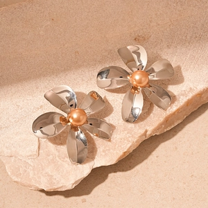 Silver flower stud earrings with orange pearl center on minimalist stone display