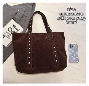 Detail of dark brown suede tote bag featuring silver studs and a heart pendant charm