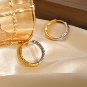 Macro detail of gold and silver two-tone hoop earrings with engraved diamond pattern