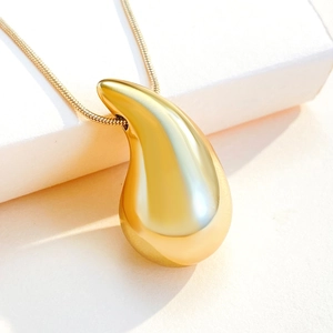 Close-up of golden teardrop pendant with fine snake chain on white minimalist base