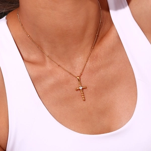 Close-up of 18K gold plated cross necklace with clear zircon stone on a bead chain