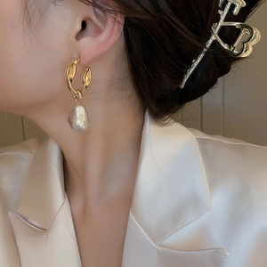 Close-up of golden irregular metal earring with a baroque pearl drop on a model