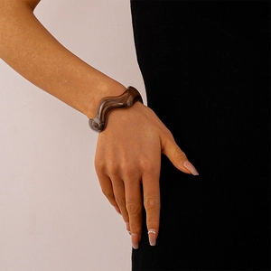 Detailed view of irregular wavy amber acrylic resin bangle on model's wrist