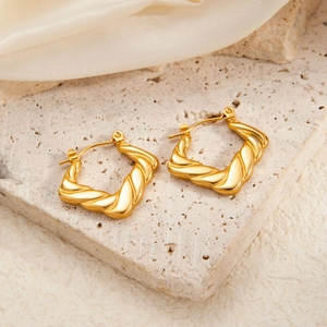 Macro view of gold-plated twisted geometric earrings on a minimalist stone display