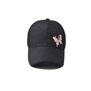 Detail of rhinestone butterfly accessory on black cotton baseball cap with textured fabric