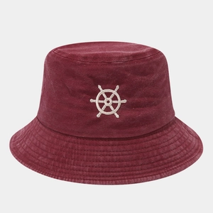 Macro detail of the embroidered white ship wheel logo on the burgundy cotton bucket hat