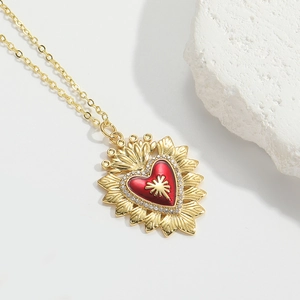 Detail of gold heart pendant with red enamel, white zircon stones, and sunburst texture