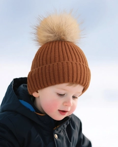 Detail of caramel knit baby hat with a large faux fur pompom for winter outdoor warmth
