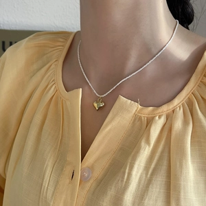 Close-up of heart pendant necklace with gold polish and white bead chain on neck