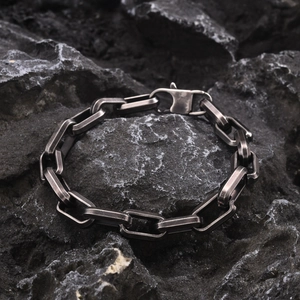 Detail of gunmetal box chain bracelet on a dark textured rock background