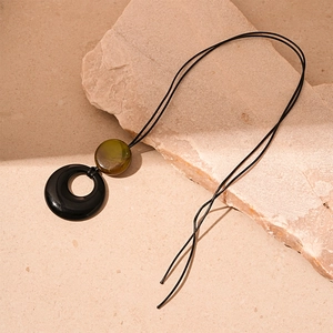 Detail of vintage resin circle pendant with green bead on black rope necklace