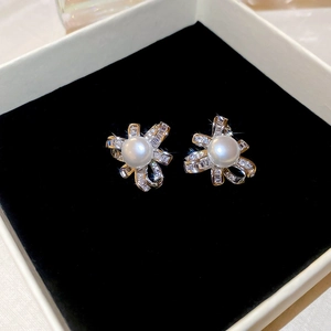 Macro detail of silver pearl earrings with sparkling zircon bow on a black velvet display