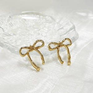 Macro shot of elegant golden bow stud earrings on a textured decorative glass plate