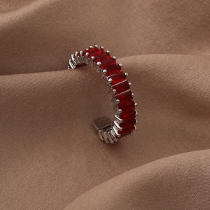 Detail of minimalist silver ring with red square zircon on brown fabric background
