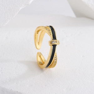 Crossed 18K gold plated ring with black enamel and zircon accents on a stone background