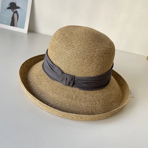 Detail of natural straw sun hat featuring a textured weave and grey knotted ribbon trim