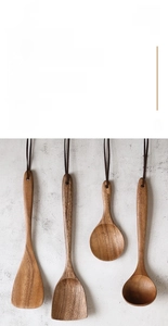 Detail of acacia wood cooking utensils with leather hanging loops on a textured wall