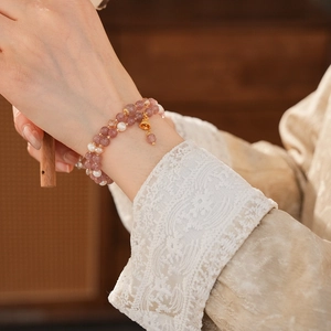 Detail of pink strawberry quartz and pearl double-layer bracelet with gold bell charm