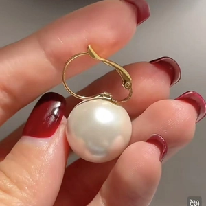 Macro detail of 14K gold plated earring with large white pearl held by hand