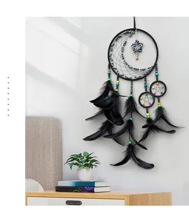 Bohemian black feather dreamcatcher with star and moon charms on a minimal white wall