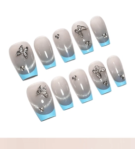 Détail d'ongles œil-de-chat bleus avec papillons métalliques argentés et strass