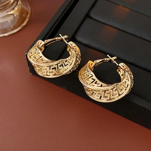 Detailed macro of gold twisted geometric hoop earrings with Greek key hollow pattern