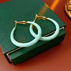 Détail de créoles vert menthe et dorées posées sur un écrin à bijoux vert foncé texturé