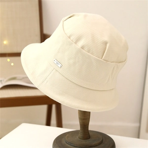 Foldable beige fisherman hat with metallic label on a wooden stand for outdoor use