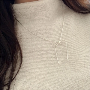 Detail of silver bow pendant on snake chain worn over a white knit sweater
