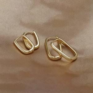 Detail view of U-shaped gold plated earrings set on a silk fabric background