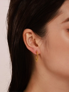 Detail of gold C-shaped sunburst earrings with beaded texture worn by a model