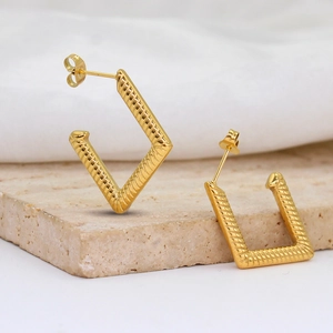 Close-up of golden geometric earrings with rope texture on a stone pedestal